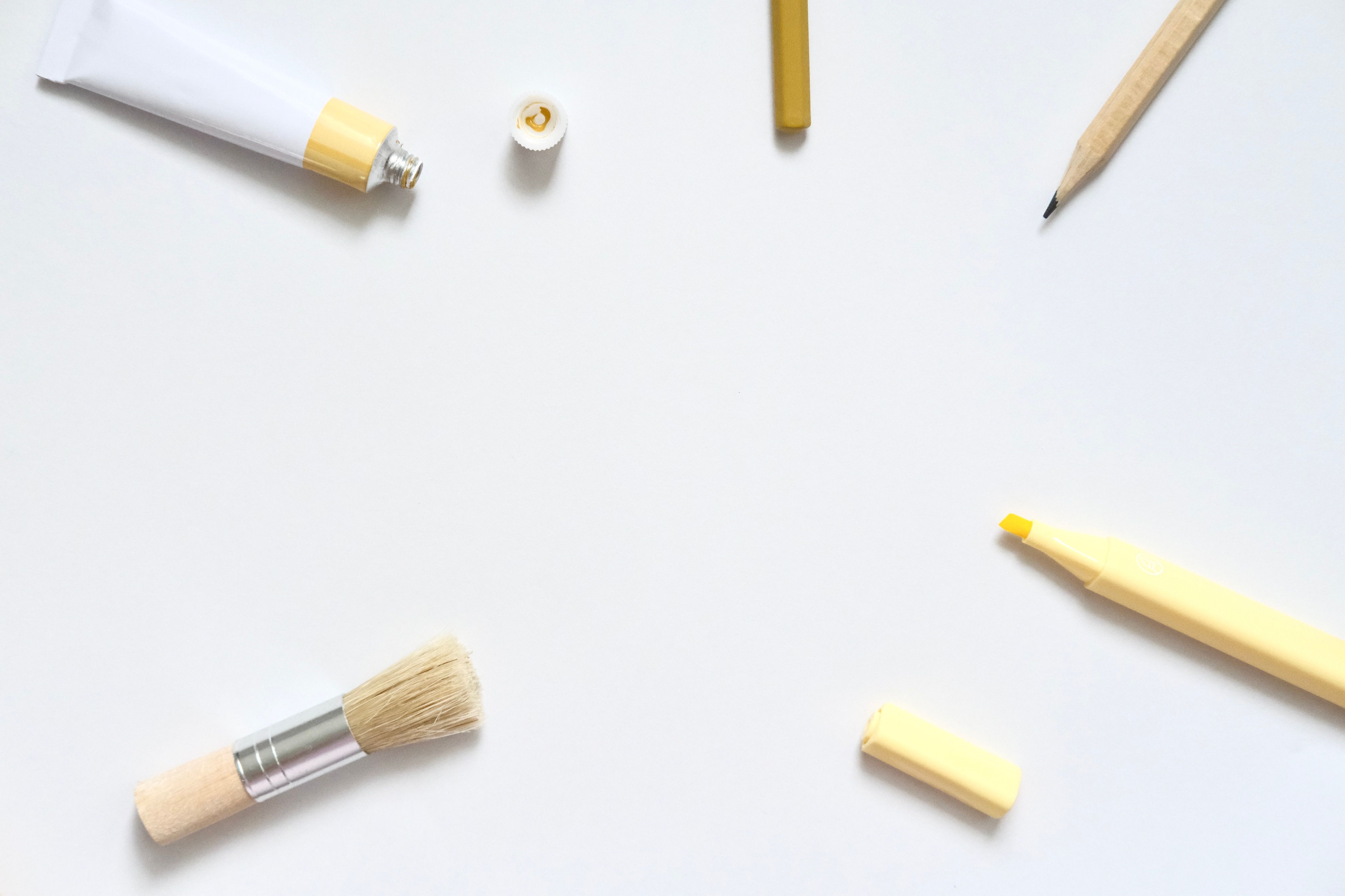 Minimalist arrangement of brushes, pencils, and paint on a white background.