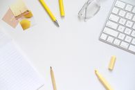 White workspace with keyboard, glasses, and yellow stationery. Perfect for productivity and minimalism themes.