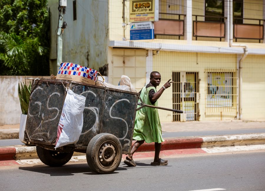 A street vendor in a green dress pushes a cart along an urban street in Lomé, Togo.