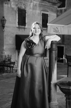 Elegant woman in a formal dress poses confidently in Kotor's historic square.