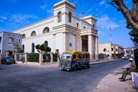 A vibrant minibus travels the streets of Dakar, passing a historic church under a clear blue sky.