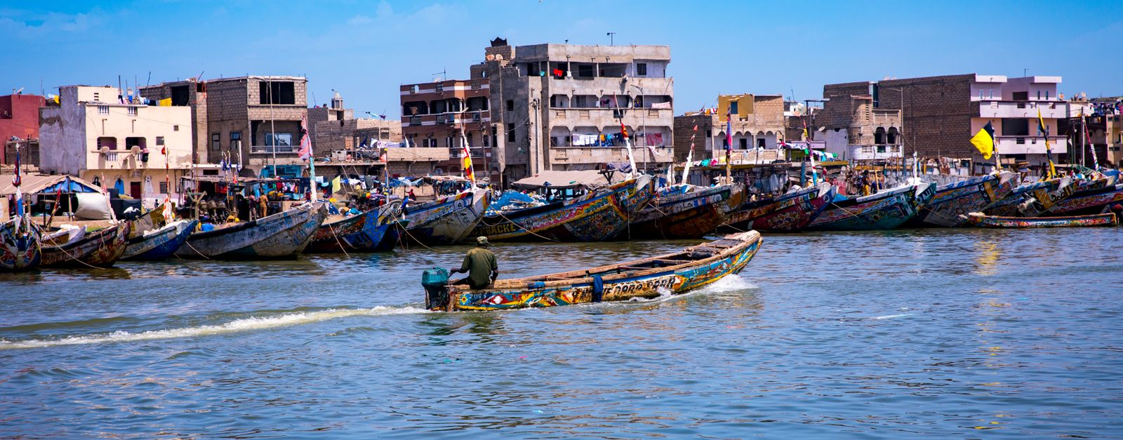 Vibrant fishing boats lined along a bustling coastal village with bright blue skies, encapsulating a lively marine scene.