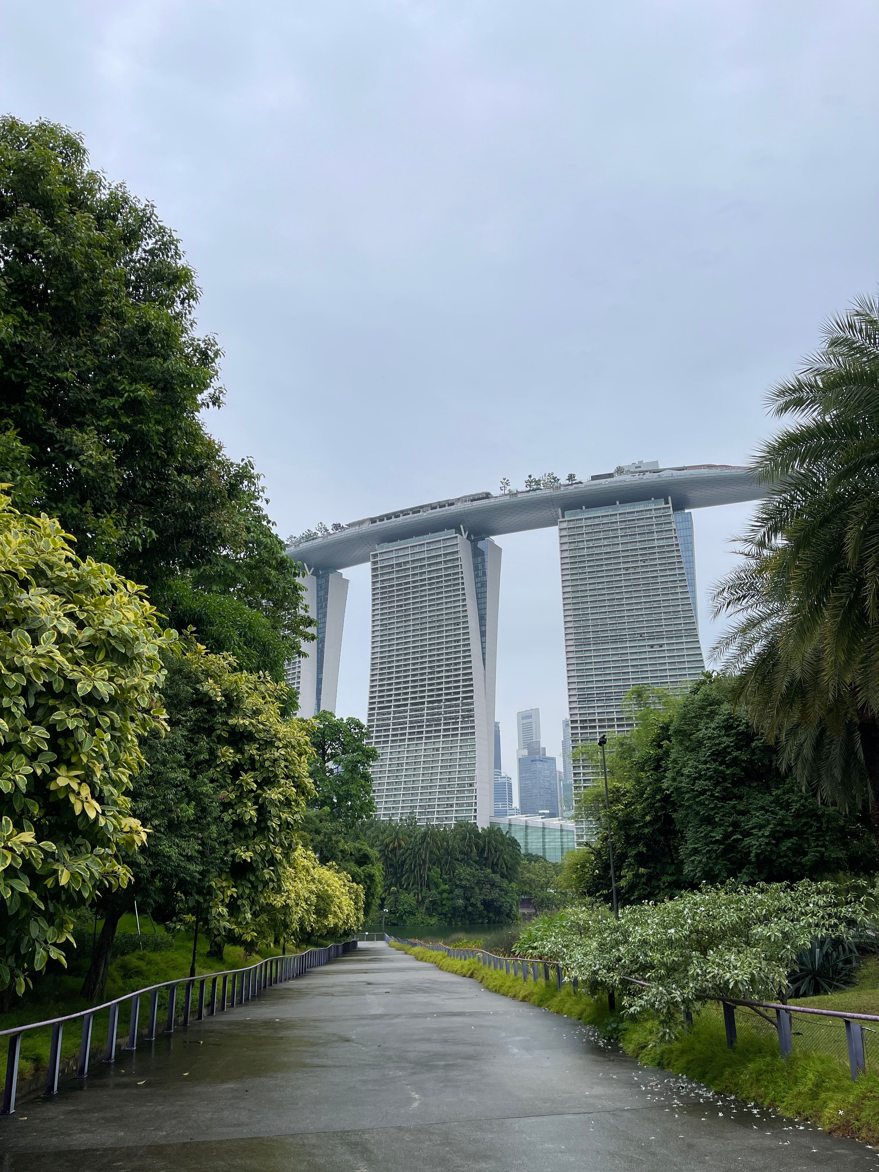 View of Marina Bay Sands from Gardens by the Bay with lush greenery on a cloudy day.