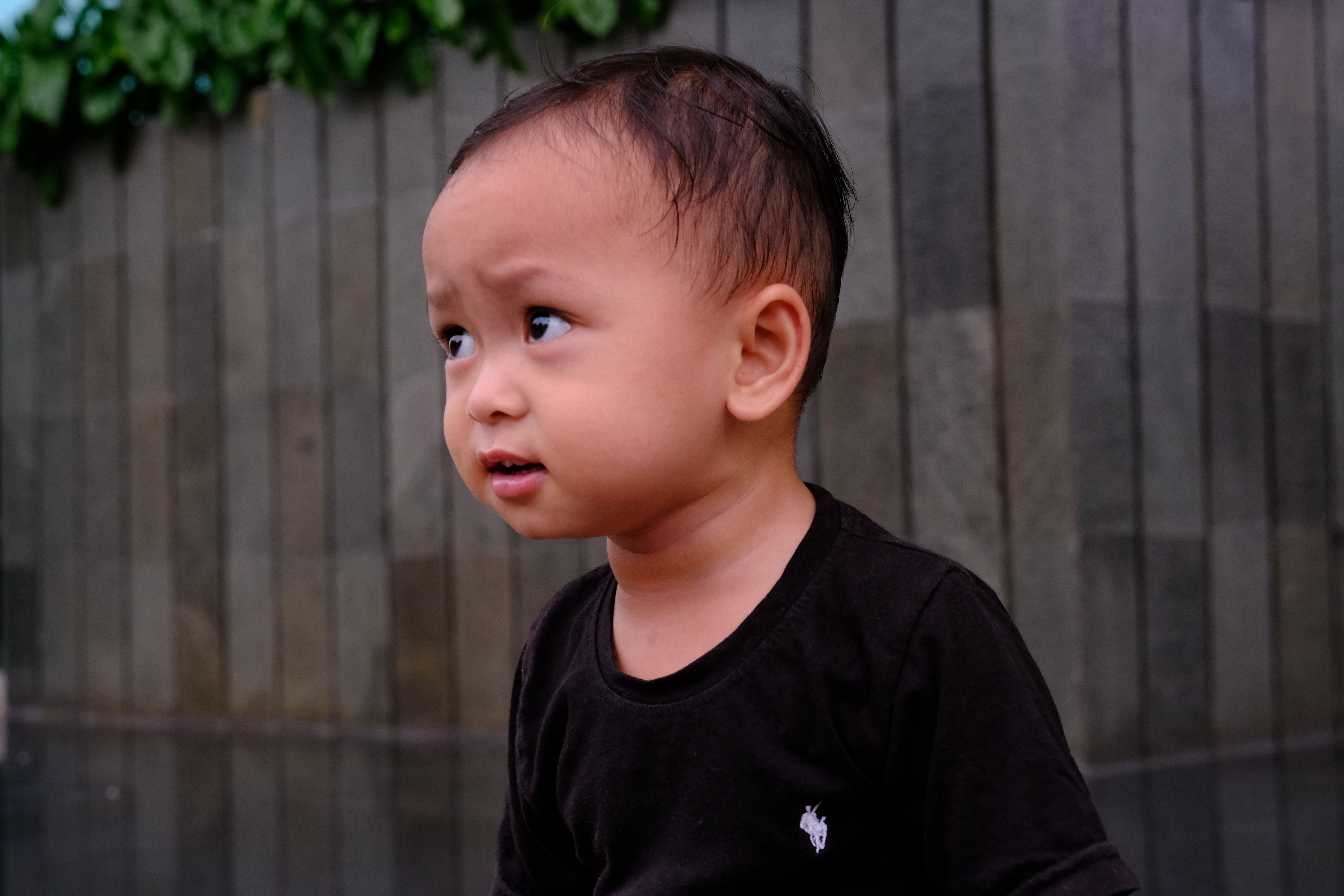A young child looking curiously to the side, outdoors against a stone wall.