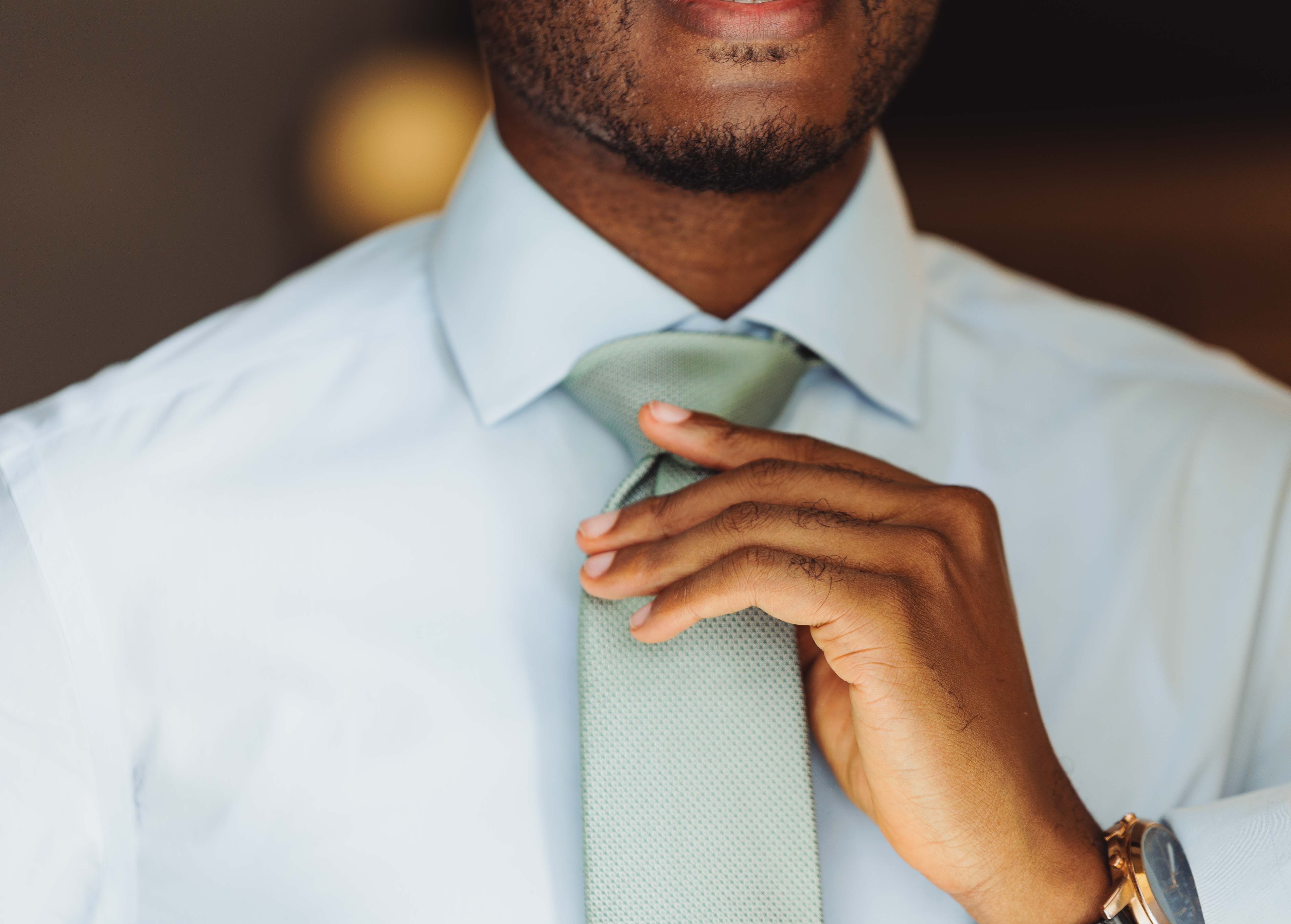Close-up of a confident professional adjusting his tie, showcasing elegance and style.