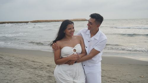 Free A happy couple embracing on a sandy beach with gentle waves in the background Stock Photo