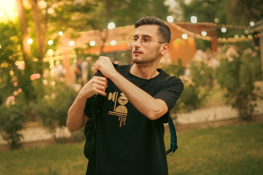 Portrait of a young man adjusting his backpack strap outside in a warmly lit park setting.