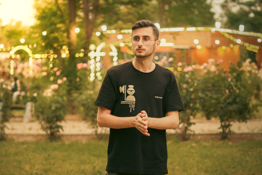 Portrait of a young man outdoors wearing a stylish black T-shirt in a garden setting with warm lighting.