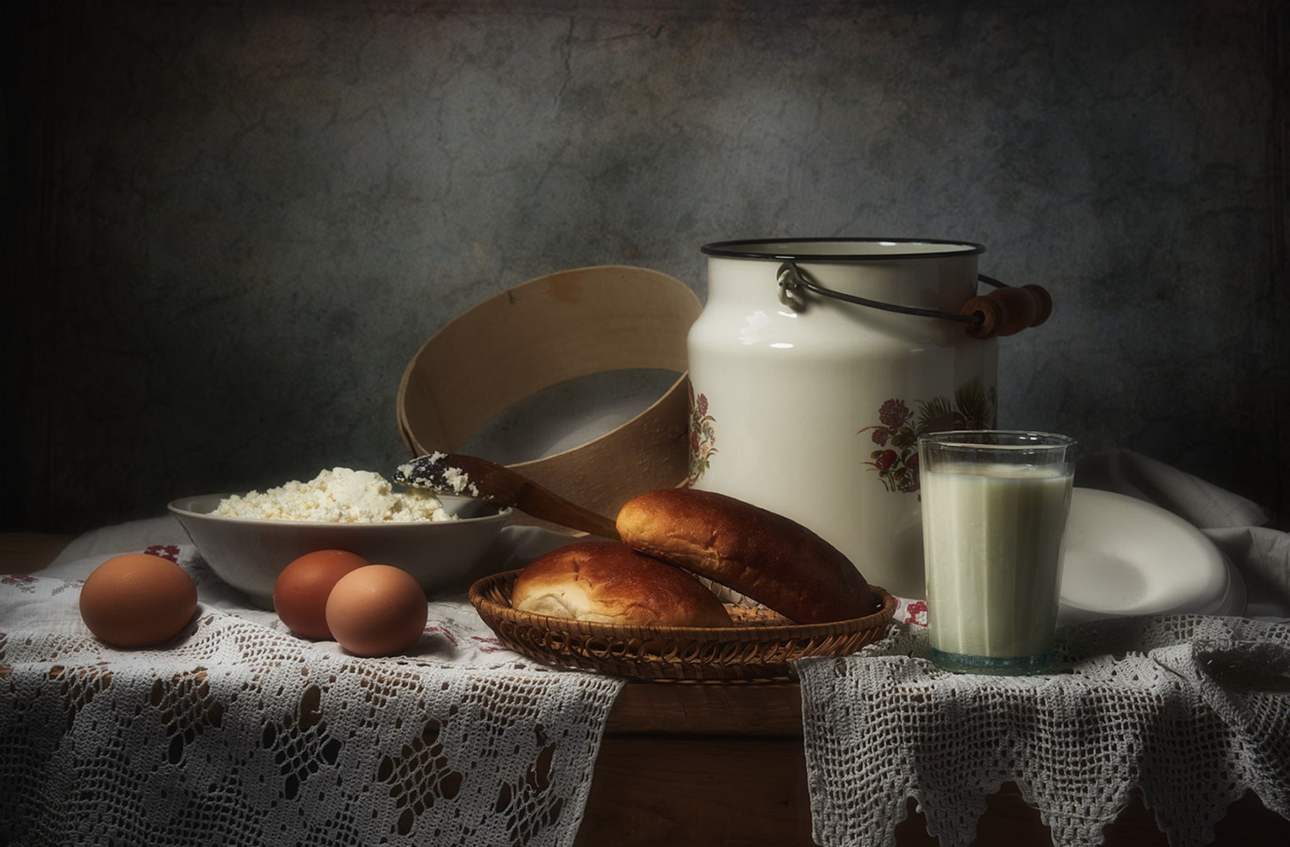 Artistic still life of cottage cheese, eggs, bread, and milk on a lace cloth.