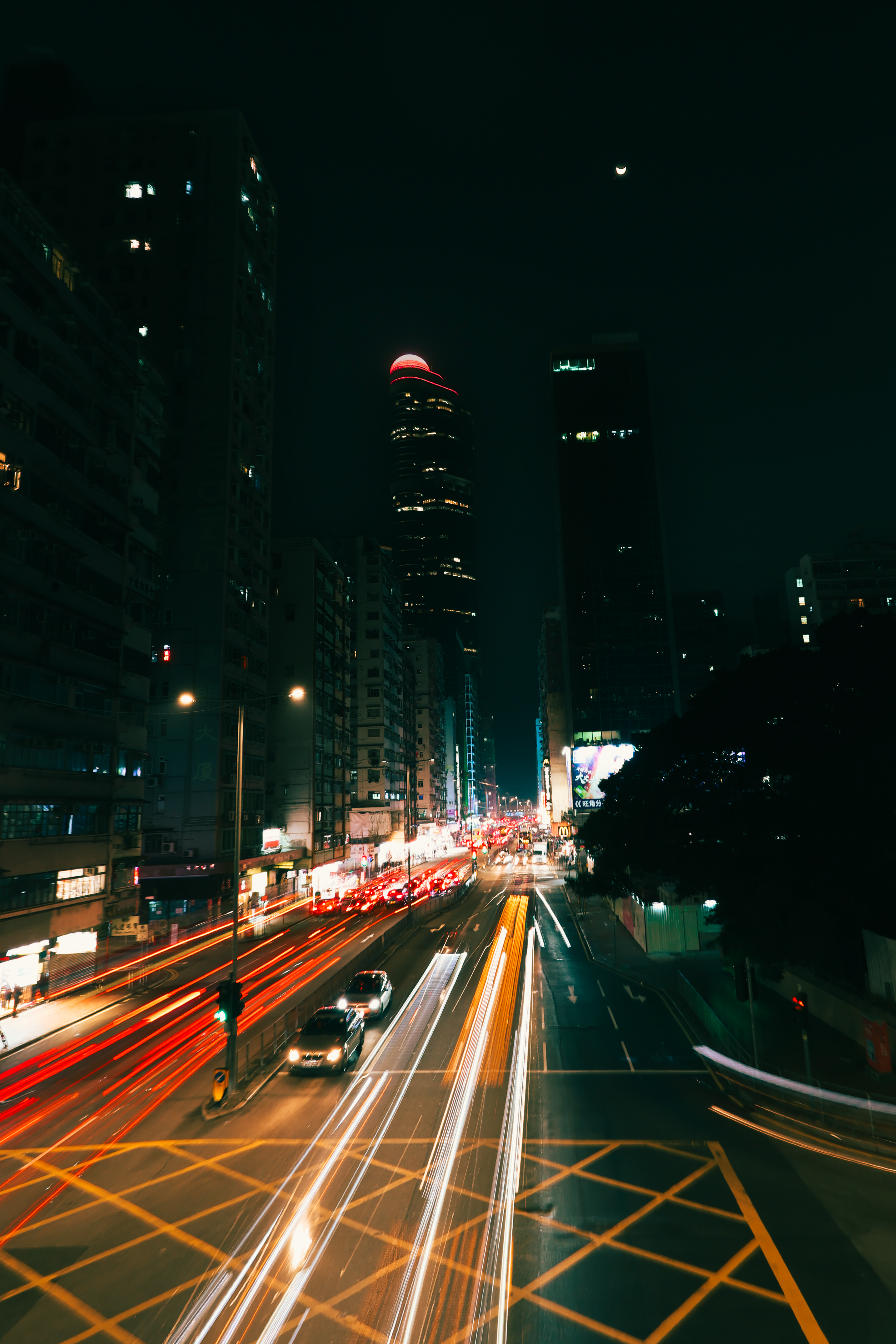 Long exposure of Kowloon's bustling night traffic, showcasing vibrant light trails and city skyscrapers.