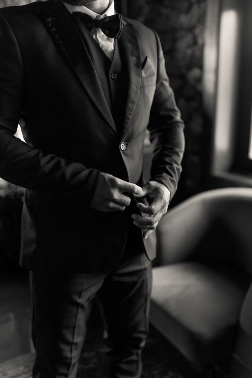 Free Man adjusting his suit coat, displaying elegance and sophistication in a stylishly furnished room. Stock Photo