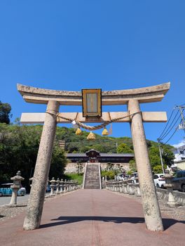A traditional torii gate leads to a serene Japanese shrine under a clear blue sky.