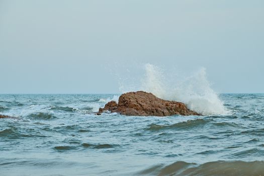Dynamic ocean waves splash against a rocky shoreline on a clear day.