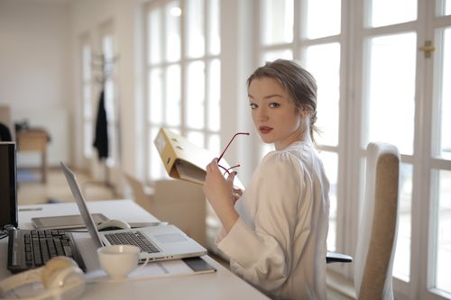 Free Back view of confident female entrepreneur in classy blouse sitting at table and doing paperwork in modern workplace while looking over shoulder Stock Photo