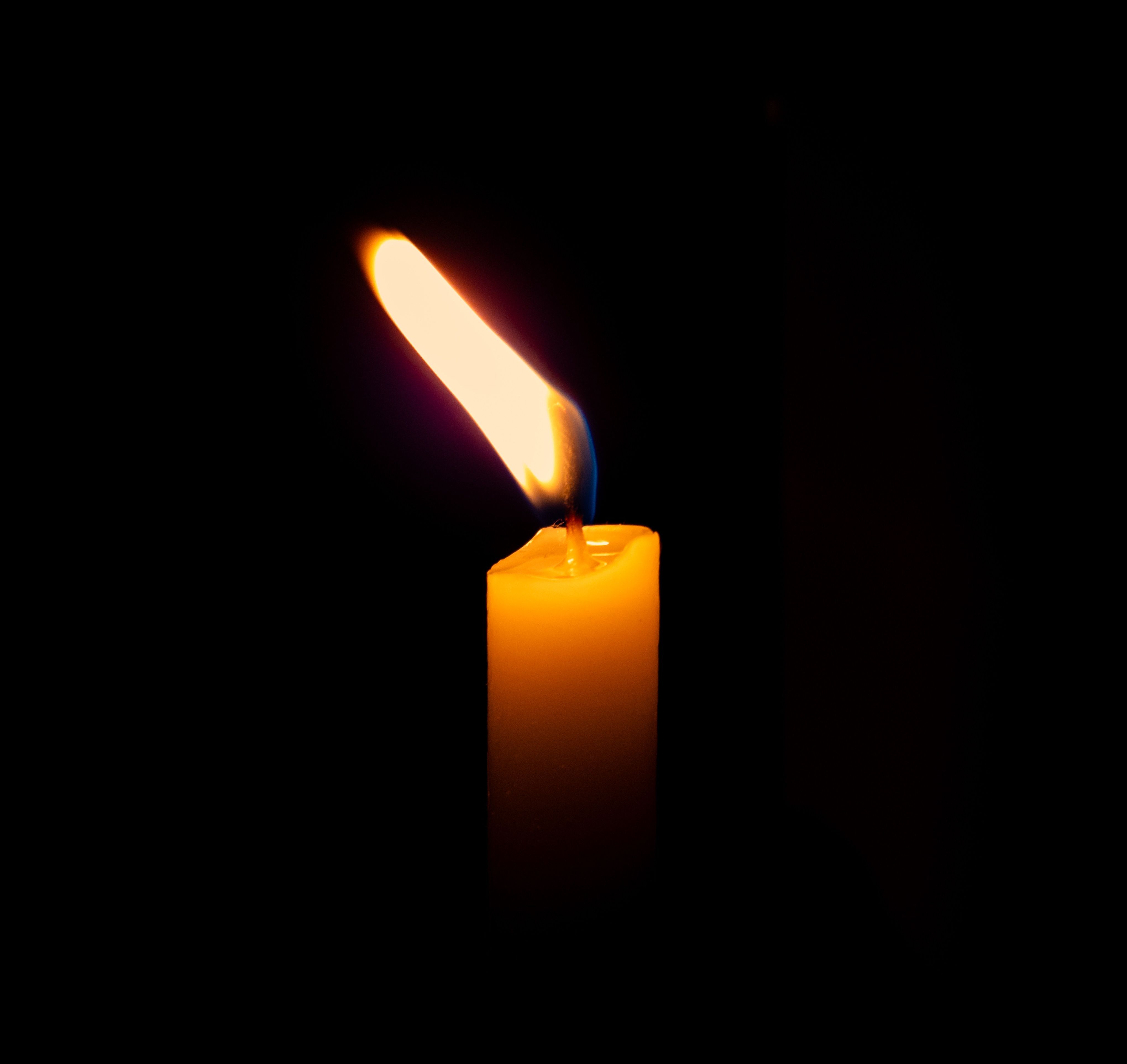 gratis Een close-up van een eenzame kaarsvlam die in het donker gloeit en een gezellige en serene sfeer creëert. Stockfoto