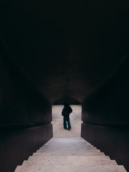 Free Silhouette of a person descending a dimly lit staircase within modern architecture in Berlin. Stock Photo