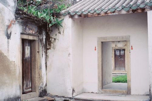Free Peaceful entryway of an ancient Asian courtyard with lush greenery and rustic wooden doors. Stock Photo