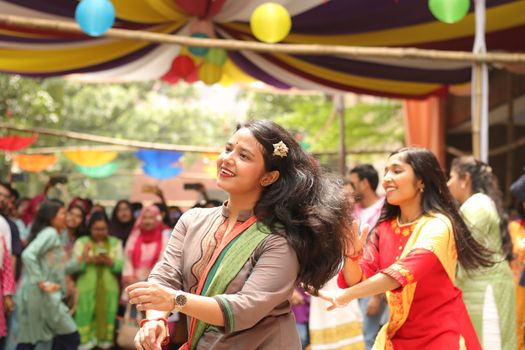 Women dancing joyfully at a colorful outdoor festival with vibrant decorations and lively atmosphere.
