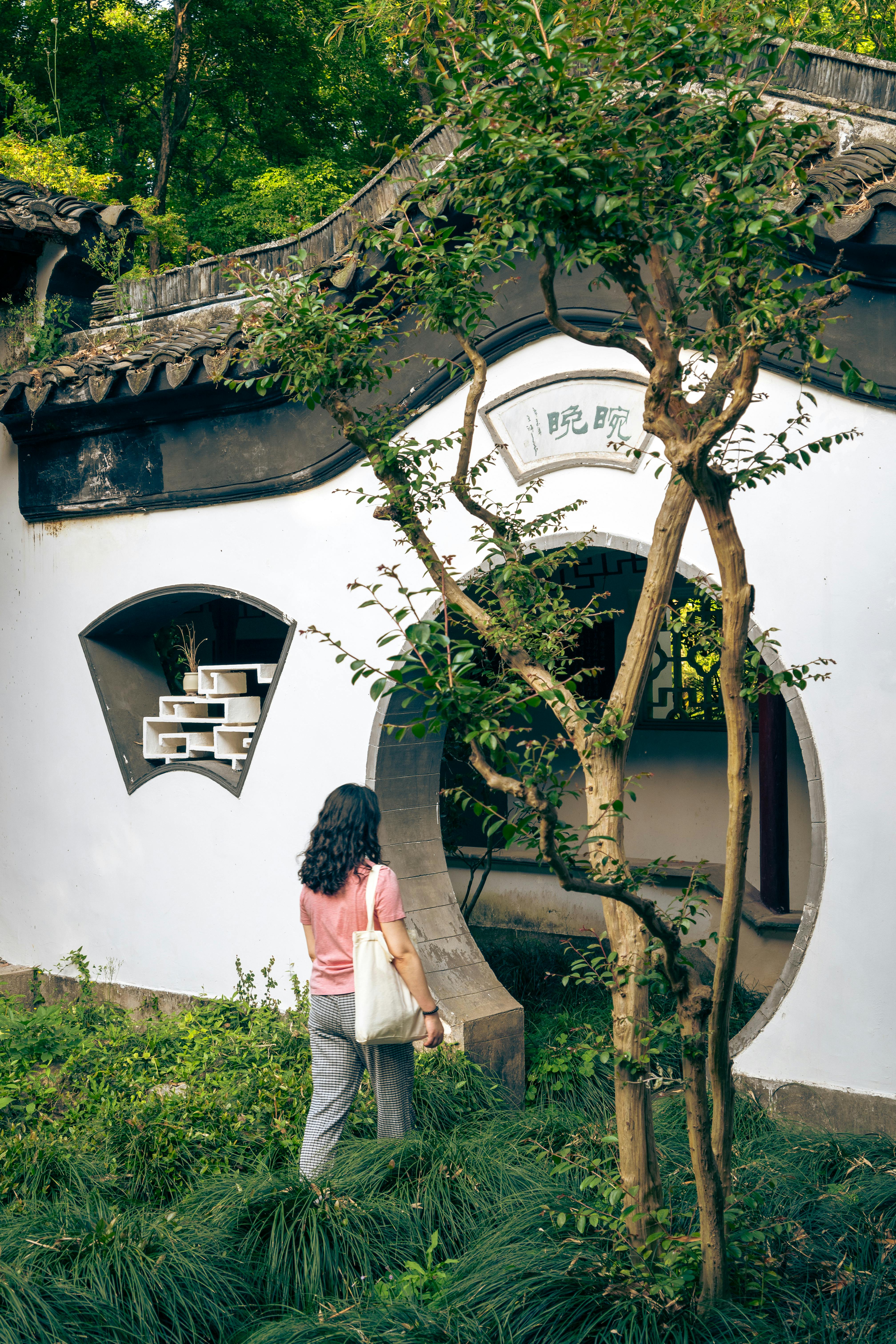 A woman explores ancient Chinese architecture in Nanjing's lush gardens.
