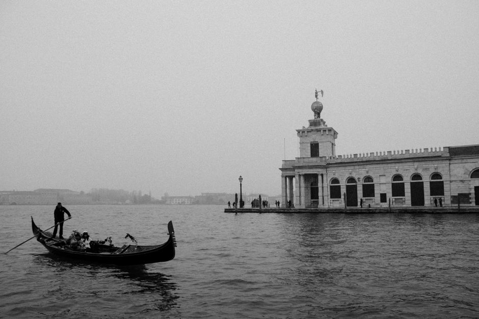 Black and white photo of a gondola on a foggy canal in Venice, Italy, with historic architecture.
