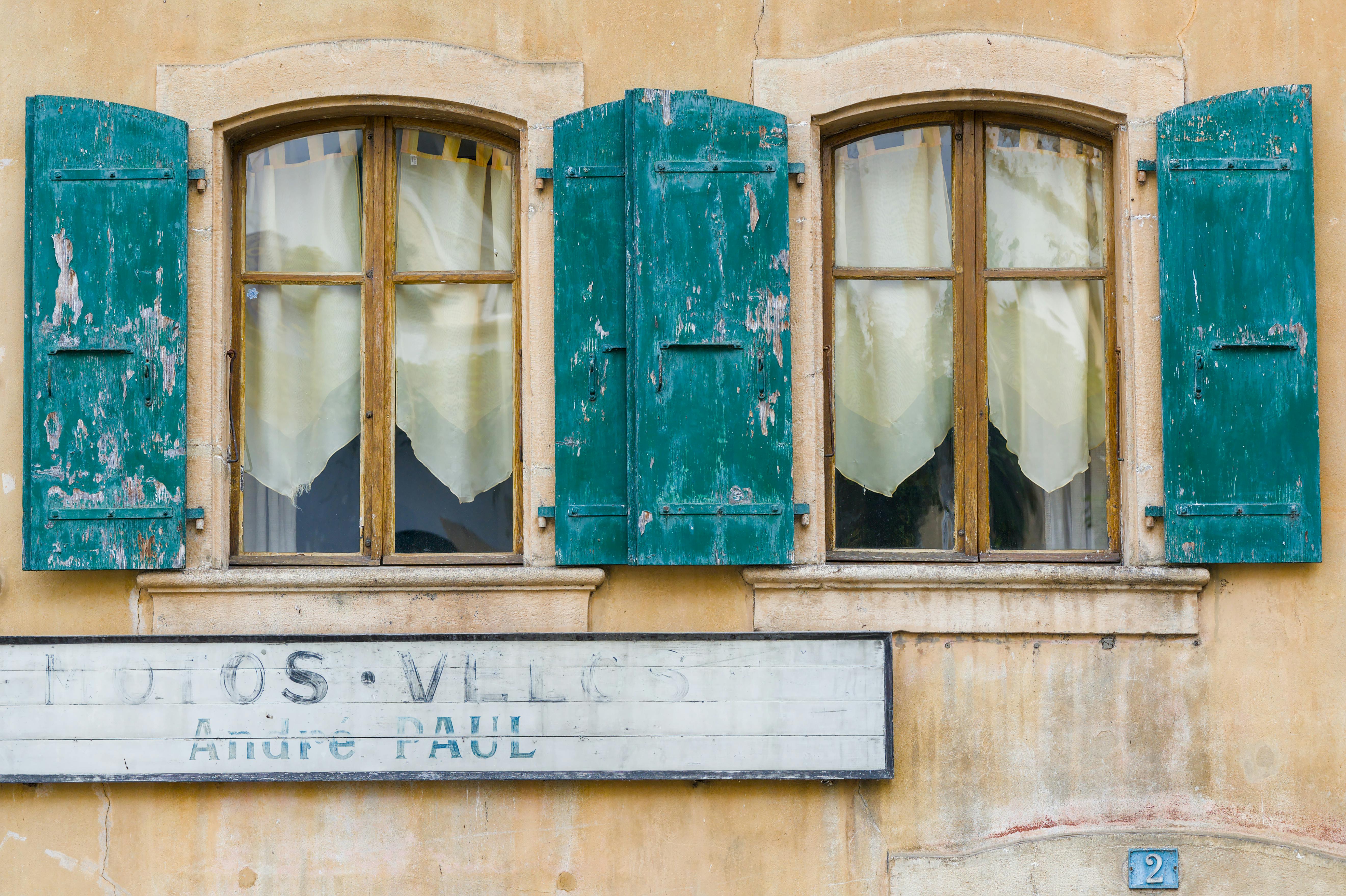Charming rustic window with teal weathered shutters in a historical building facade.