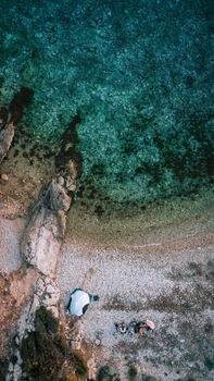 Aerial shot capturing a serene rocky beach scene with vibrant turquoise waters and a white umbrella setup.