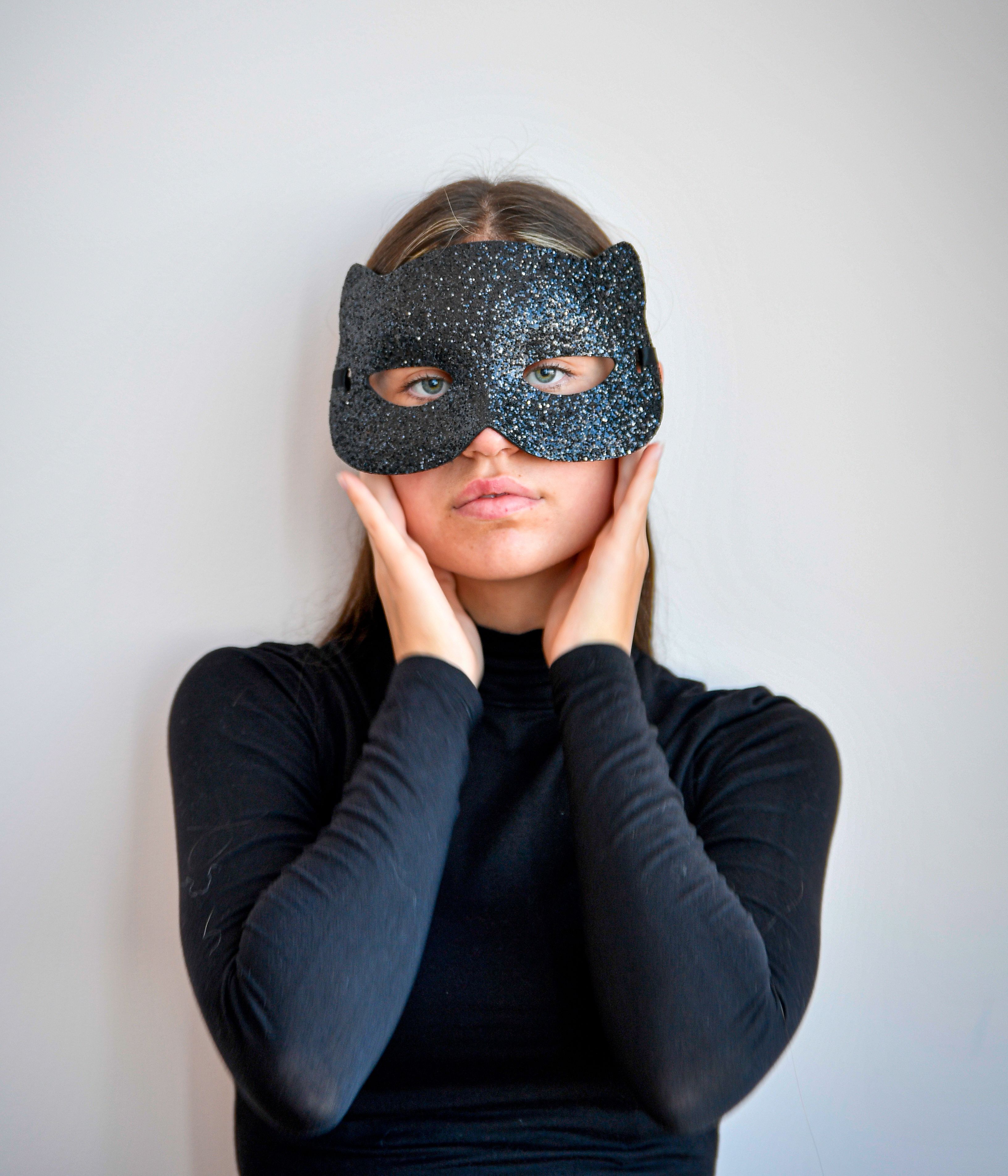 Graceful young woman in a black mask posing elegantly against a minimalistic backdrop. Mysterious and stylish.