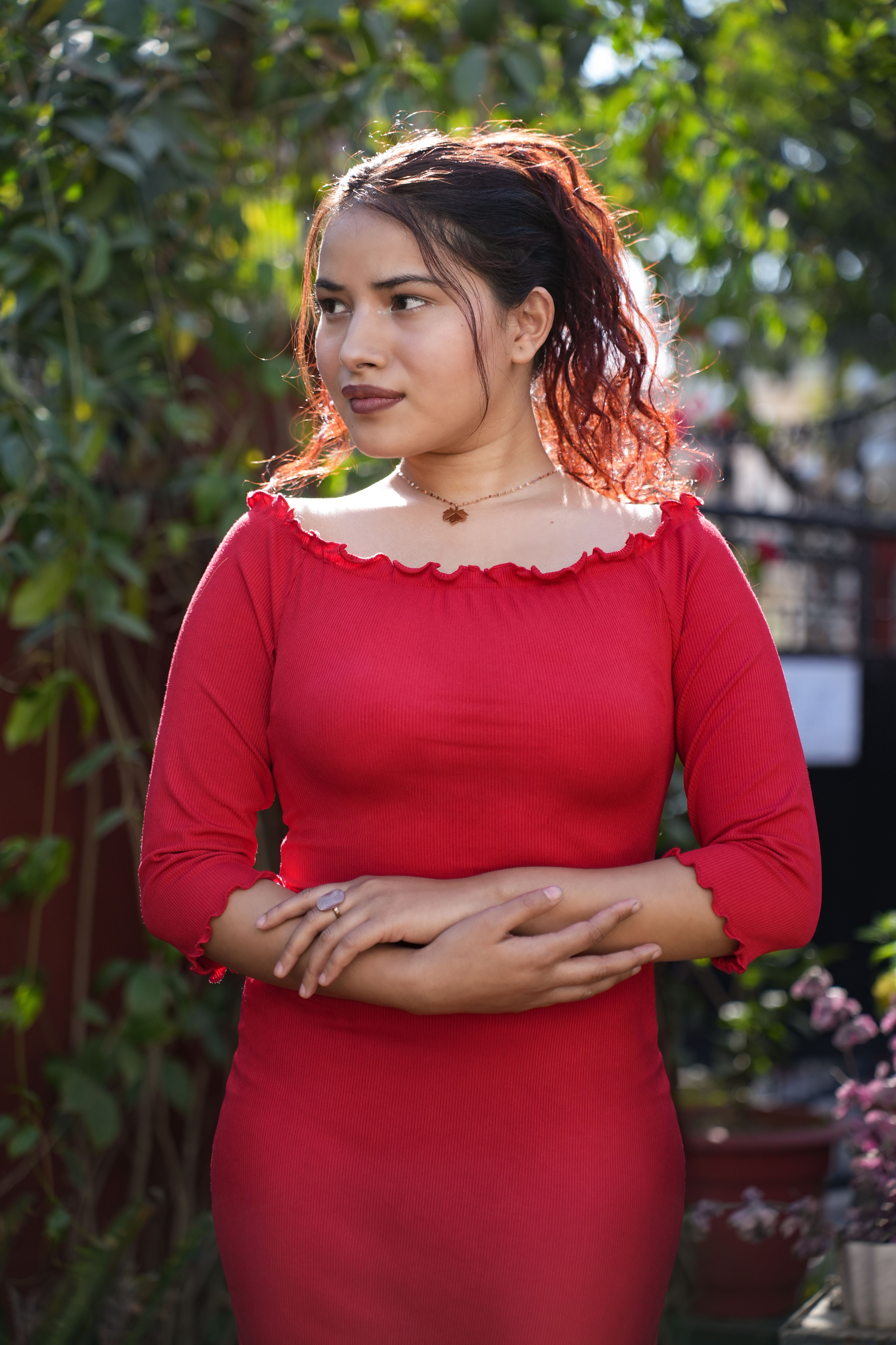 Woman in a stylish red dress standing gracefully outdoors in a lush garden.