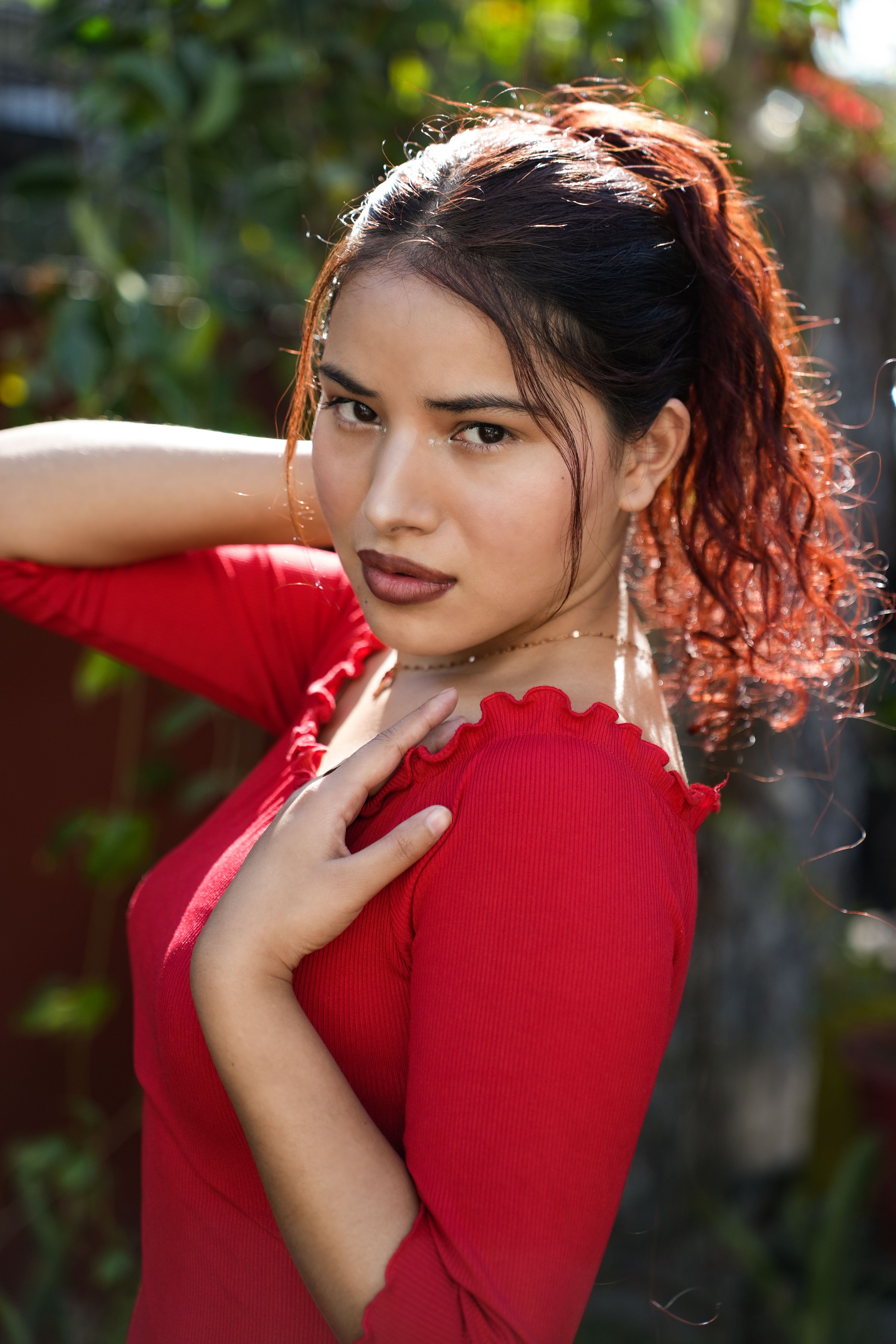 Glamorous portrait of a young woman posing outdoors in a red dress, captured in daylight.