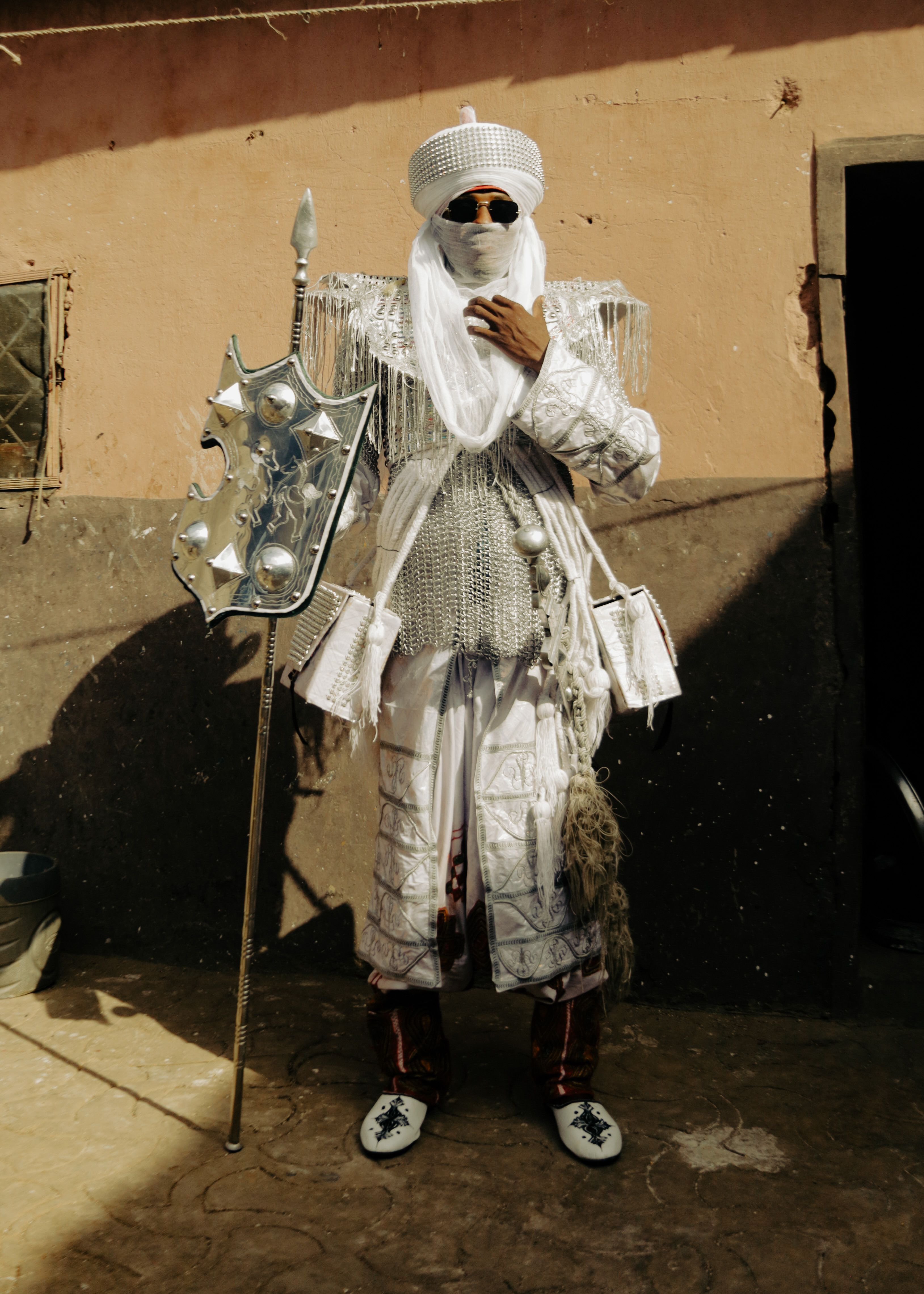 Person in traditional armor with shield stands outdoors in sunlight.