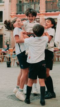 Group of happy children playing and lifting their friend in a lively Seville, Spain plaza.