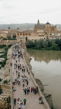 Crowd crossing the historic Roman Bridge in Córdoba with stunning historic architecture in the background.