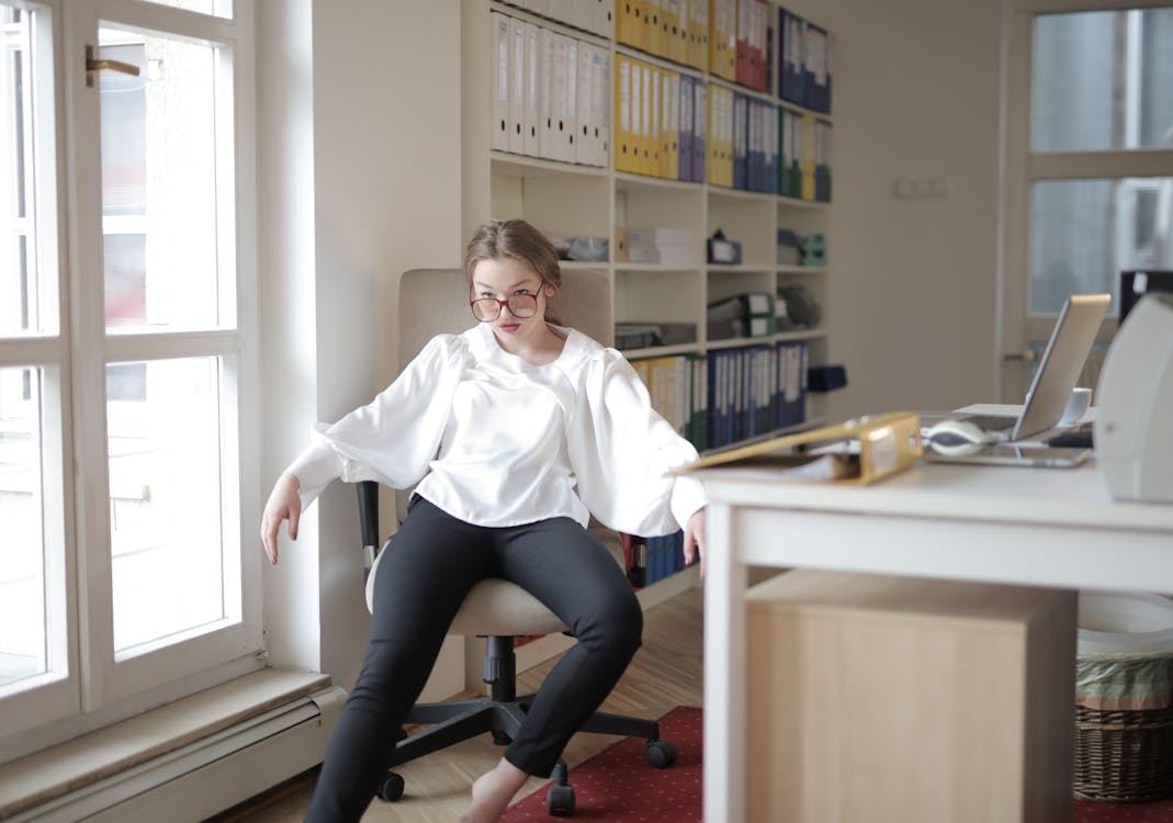 Bossy female employee in formal wear sitting on chair in workplace and demonstrating frivolous and unprofessional behavior while looking away