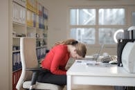 Woman in Red Long Sleeve Shirt Sitting on Chair While Leaning on Laptop