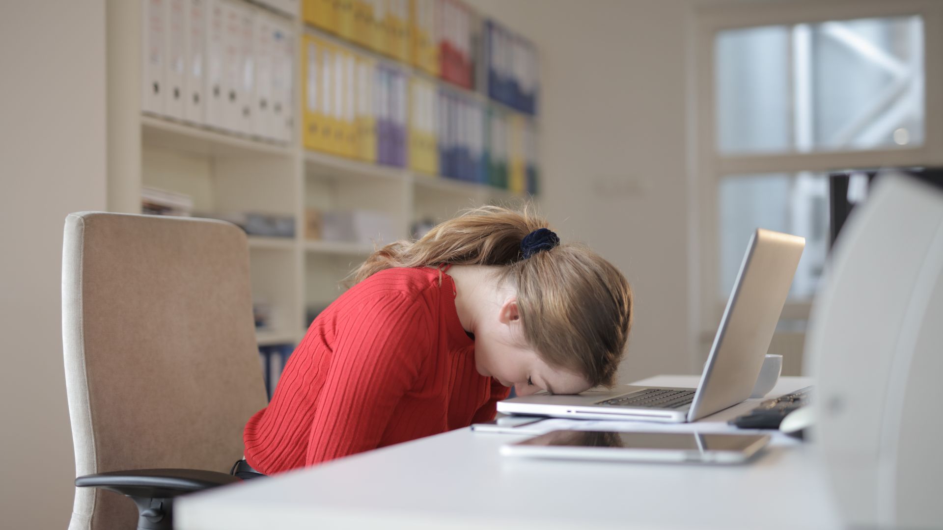 shift work sleep disorder treatment: Effective Strategies for a Better Night's Rest A tired woman in a red sweater leans her head on a desk with a laptop, symbolizing workplace fatigue — shift work sleep disorder treatment