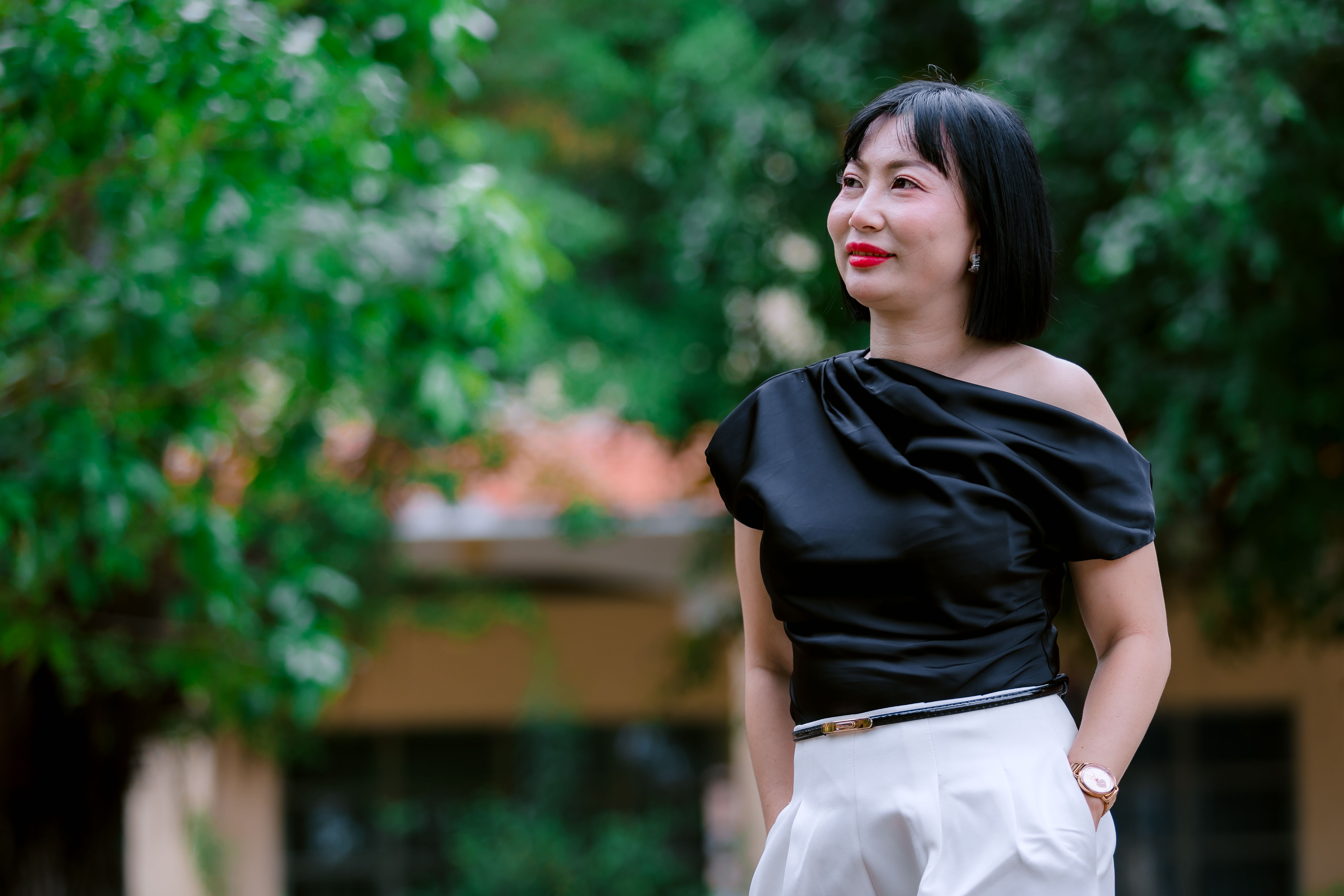 Confident woman in an elegant black top posing outdoors, surrounded by greenery.