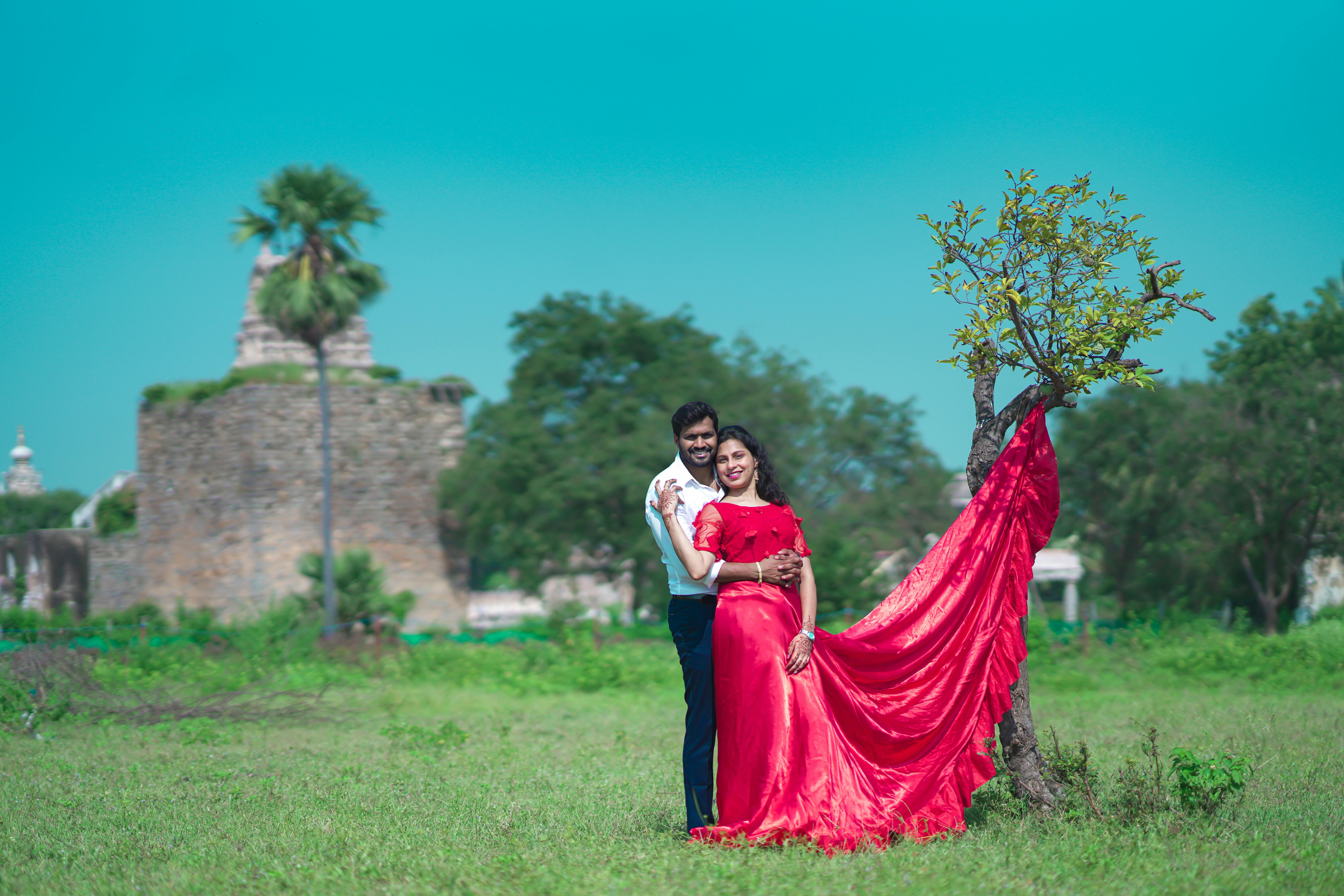Couple embracing in a vibrant red dress with Golconda Fort in the background.