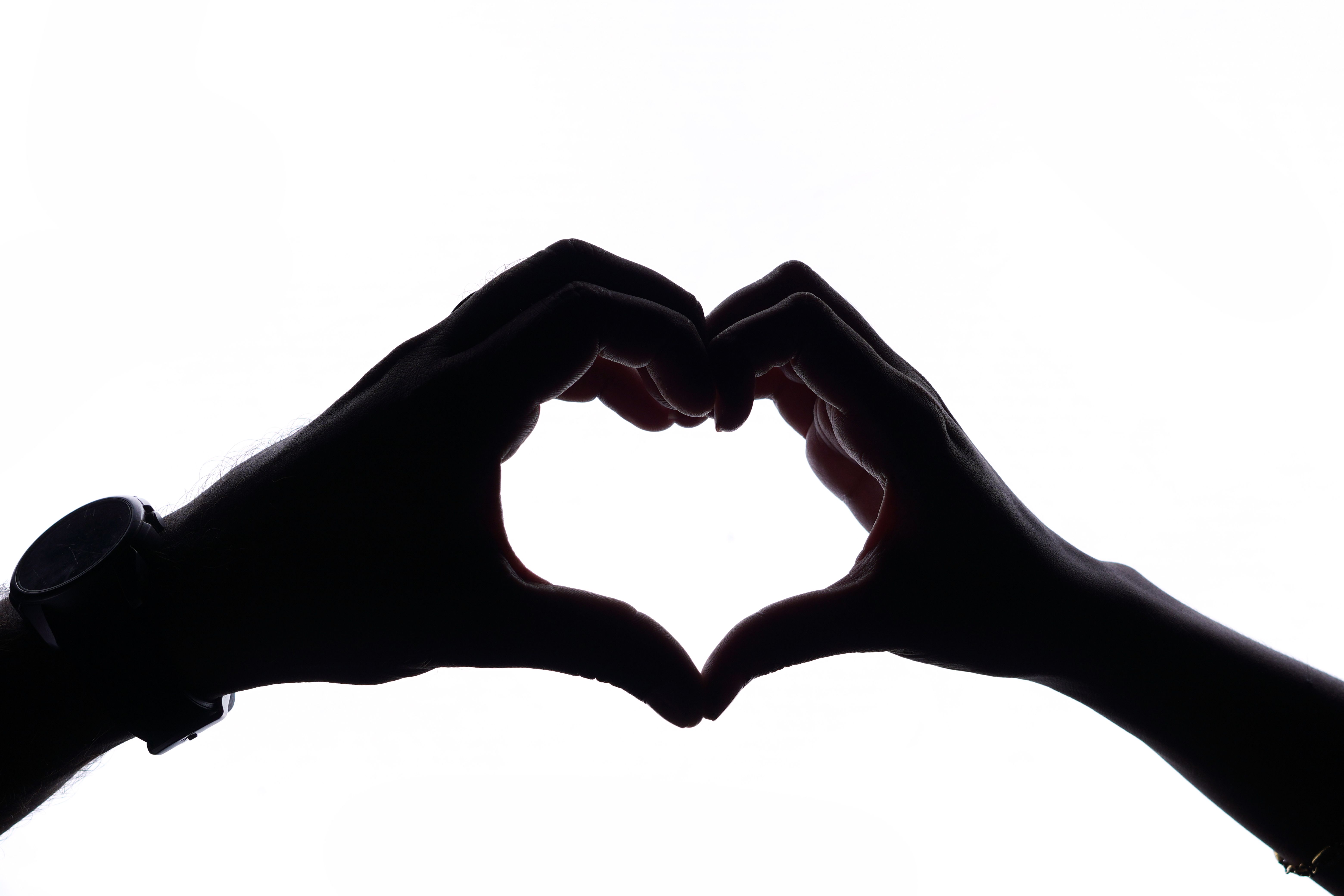 Artistic silhouette of hands forming a heart shape on a white background.