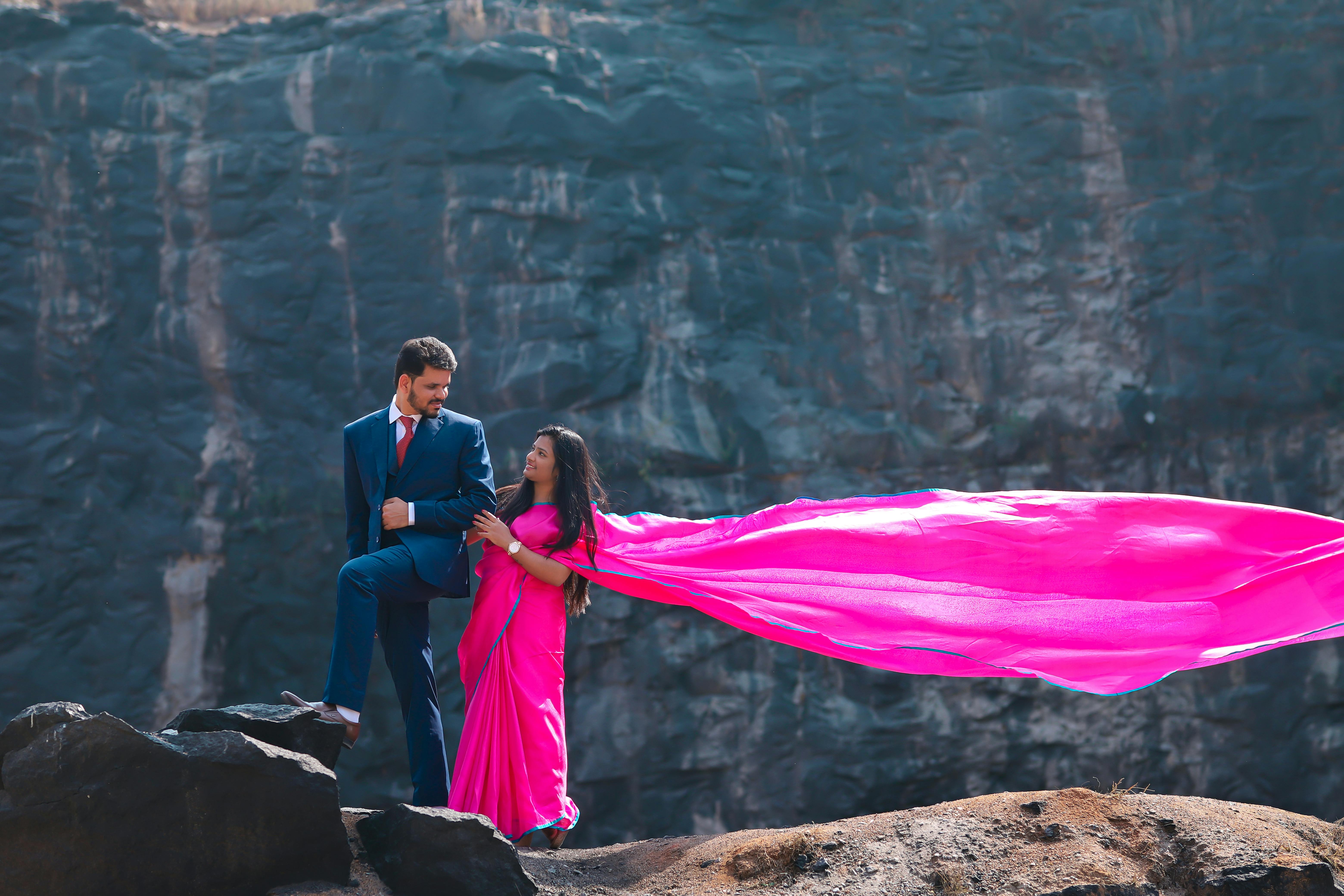 Charming pre-wedding photo of an Indian couple in vibrant attire amidst a rocky backdrop.