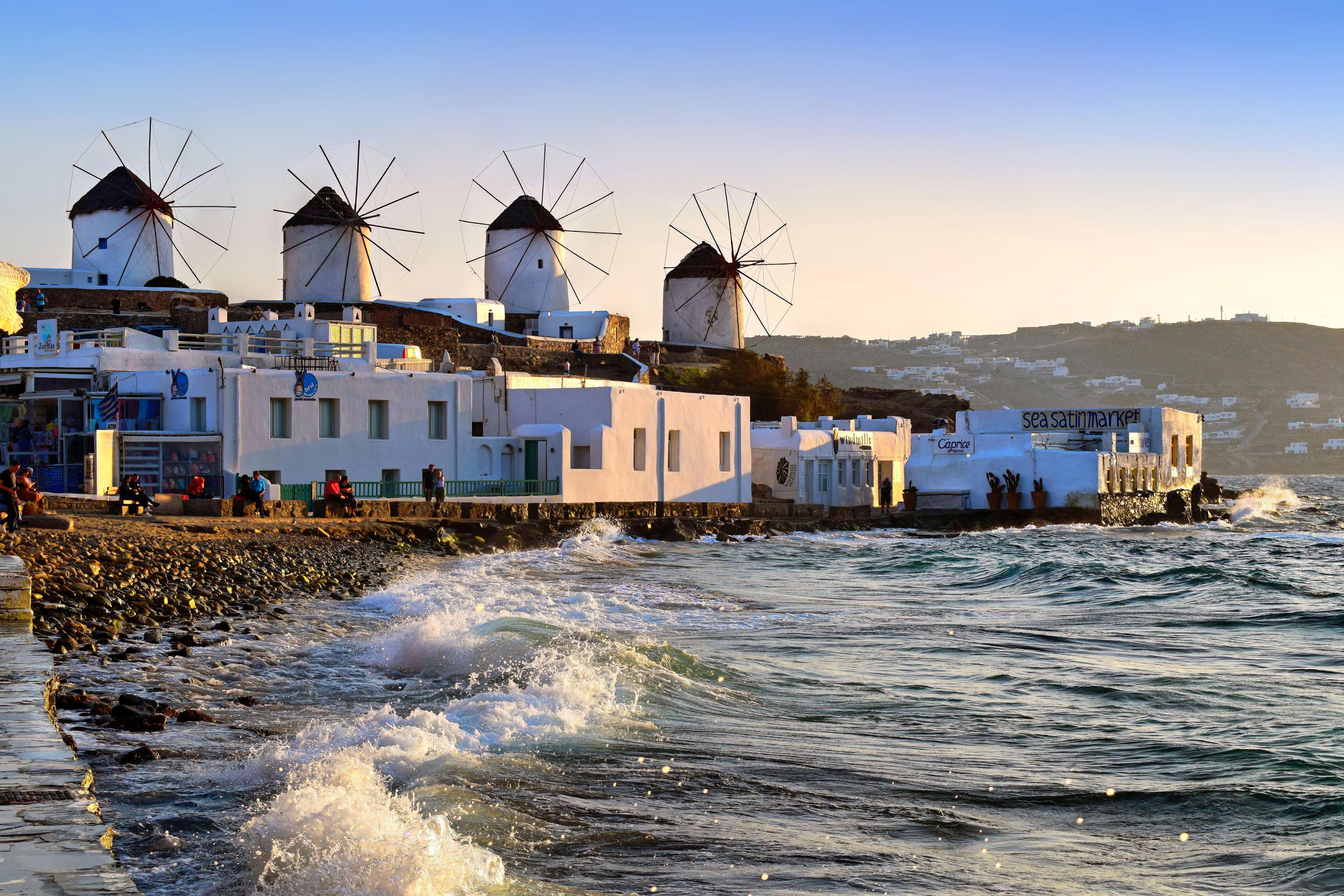 Row of whitewashed windmills on the hill above Mykonos Town glowing at sunset over the Aegean Sea