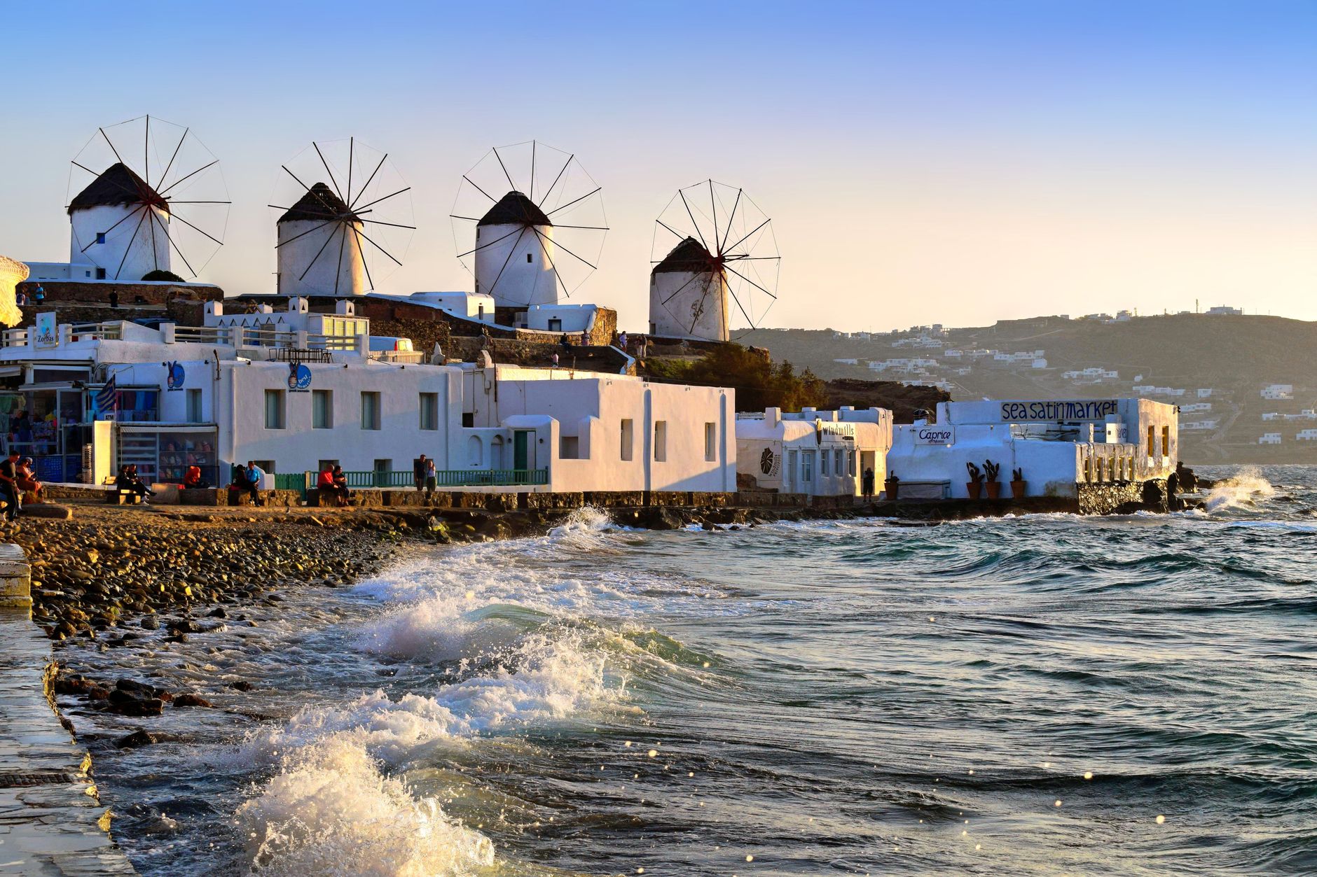 Row of whitewashed windmills on the hill above Mykonos Town glowing at sunset over the Aegean Sea