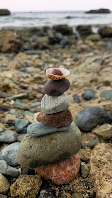 Fotomural Un mojón de piedras en perfecto equilibrio sobre una playa rocosa junto al océano, que muestra tranquilidad y el arte de la naturaleza.