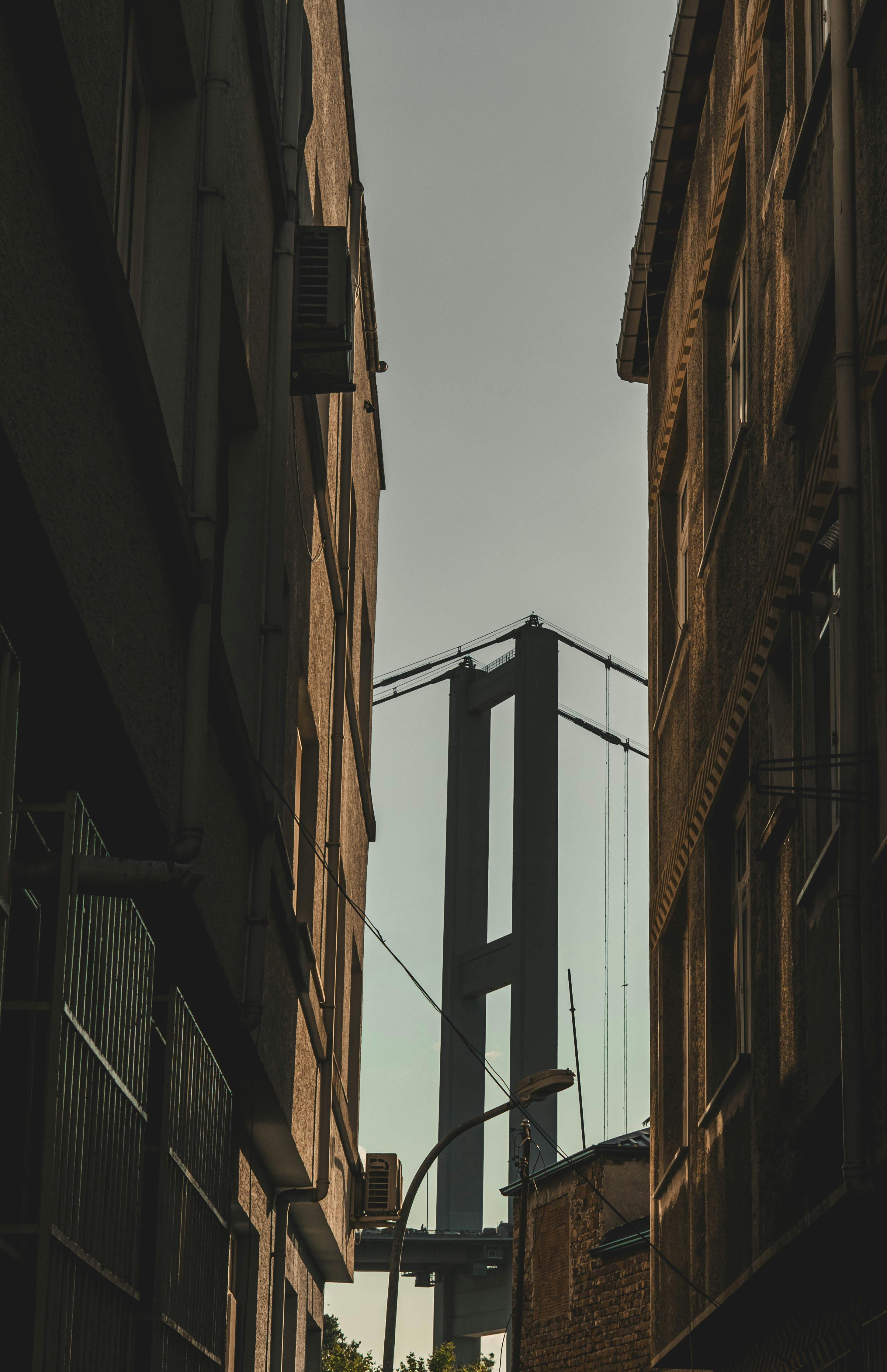 View of the iconic Bosphorus Bridge framed between buildings in İstanbul, Türkiye, during the day.