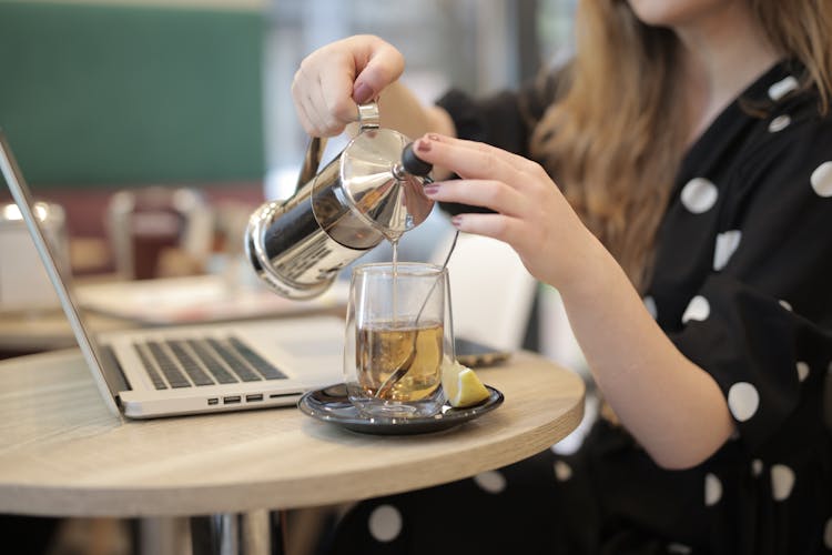 Woman Pouring Hot Tea From French Press Into Glass Cup