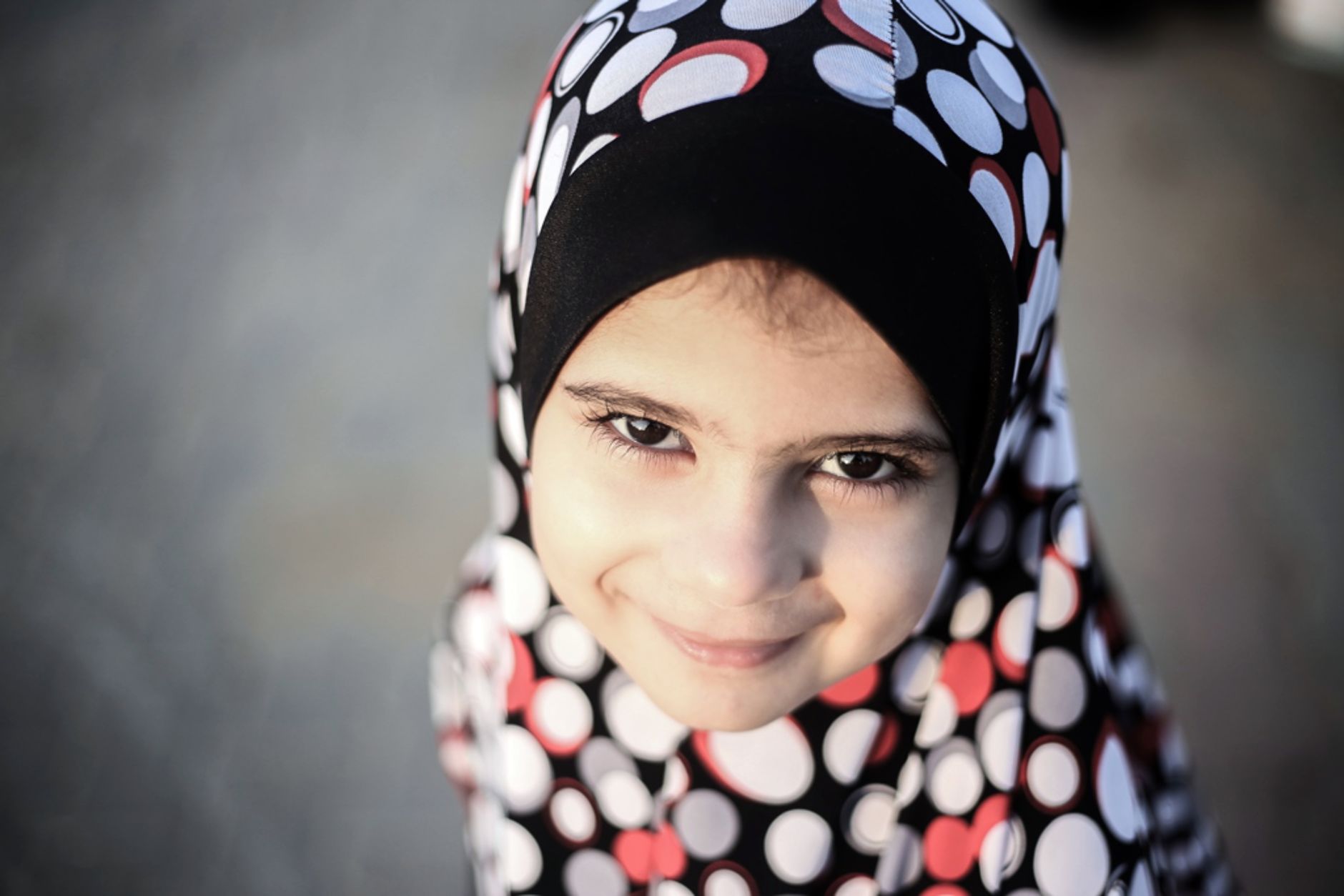 Portrait of a smiling young girl wearing a colorful polka dot hijab outdoors.