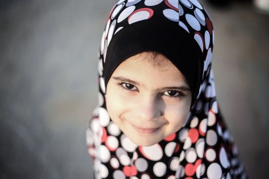 Portrait of a smiling young girl wearing a colorful polka dot hijab outdoors.
