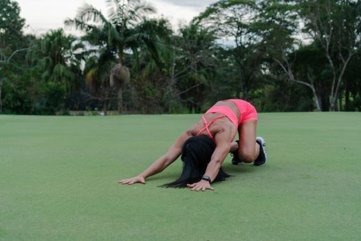A woman in vibrant attire performing yoga outdoors on green grass.