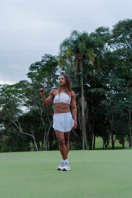 Photo by Wolf Art Confident athletic woman holding a golf club on a lush green golf course, surrounded by trees.