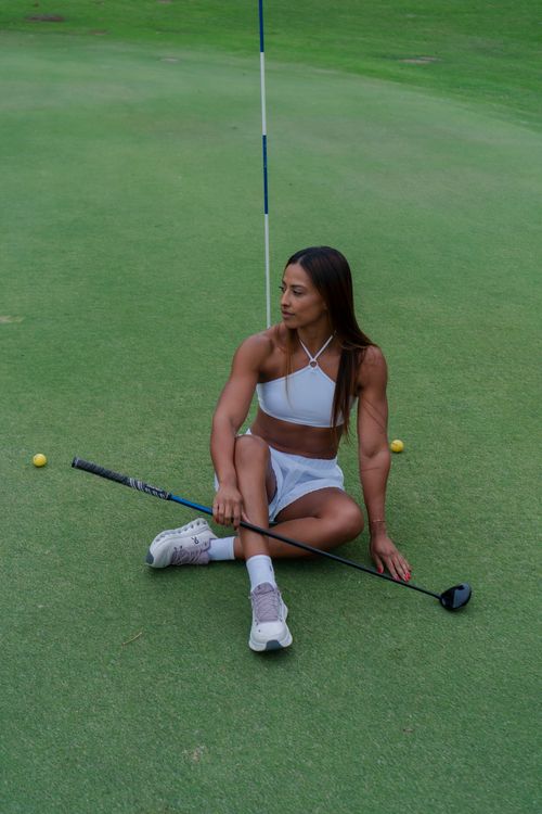 Free Athletic woman sitting on green with golf club, exuding calm elegance and style. Stock Photo