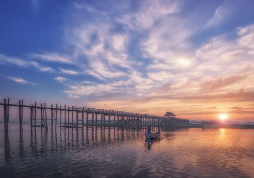 Picturesque sunrise over U Bein Bridge with calm reflective waters and scenic sky.